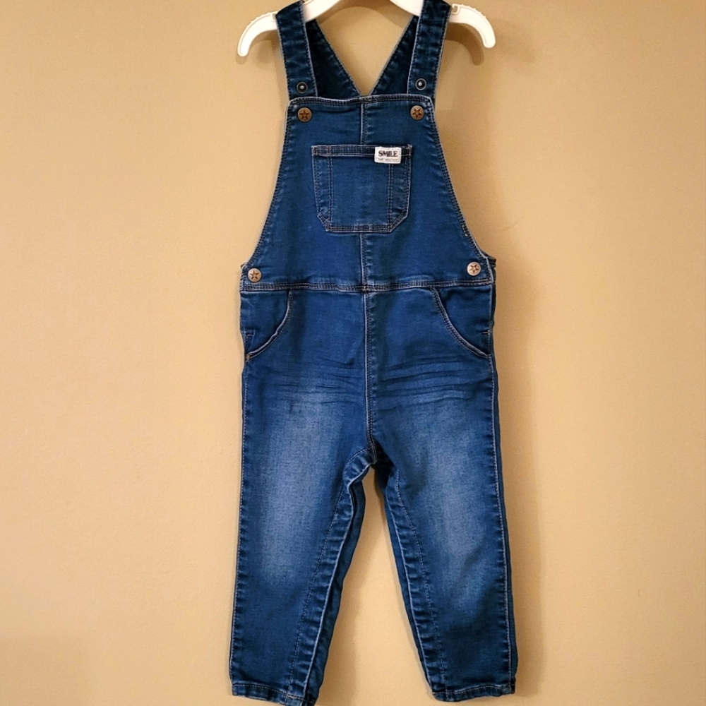 Medium wash denim overalls with "Smile" patch